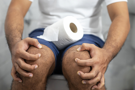Man with a toilet paper sitting on a toilet.