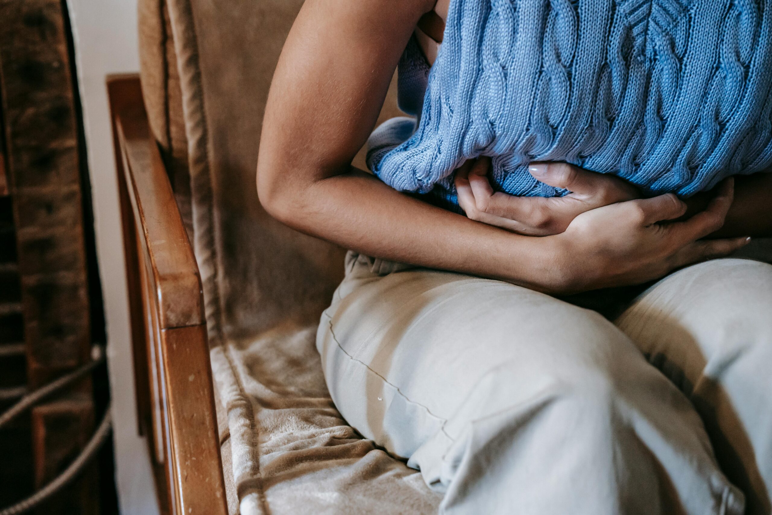 Woman sitting on a chair holding her stomach due to pain.