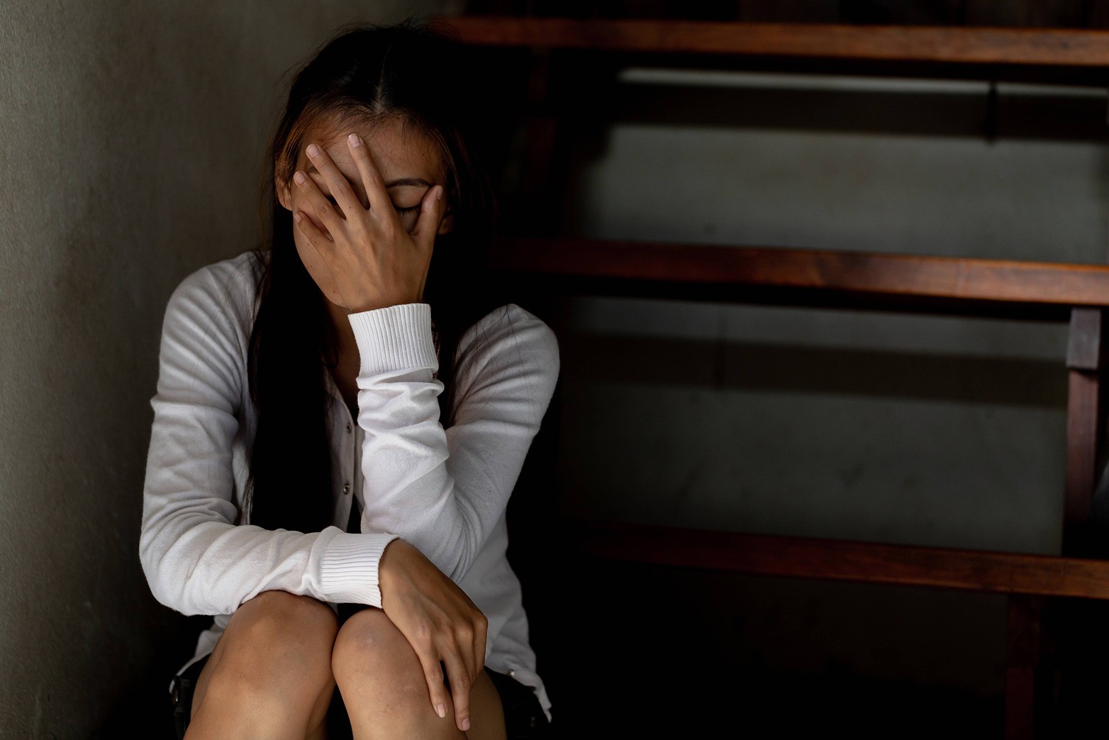 Sad woman sitting on the stairs covering her face with her hand.