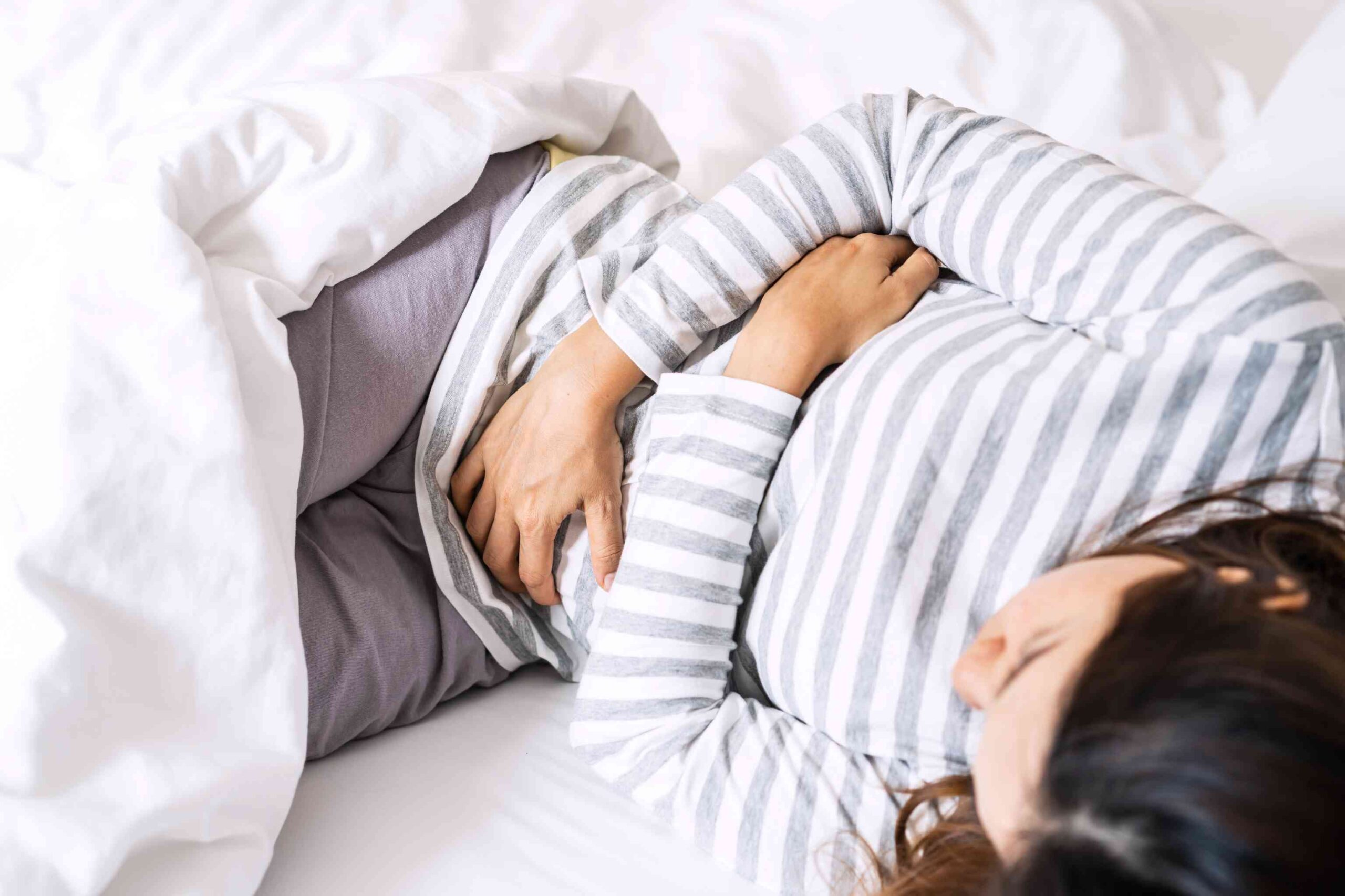 A woman lying on a bed holding her stomach.